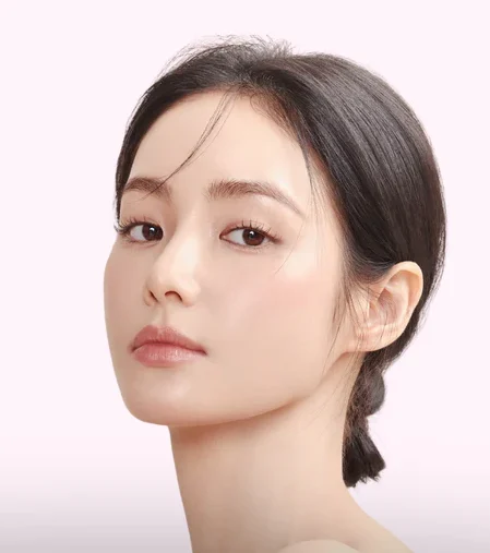 Close-up portrait of a young woman with dark hair in a low bun, gazing softly at the camera against a pale pink background.